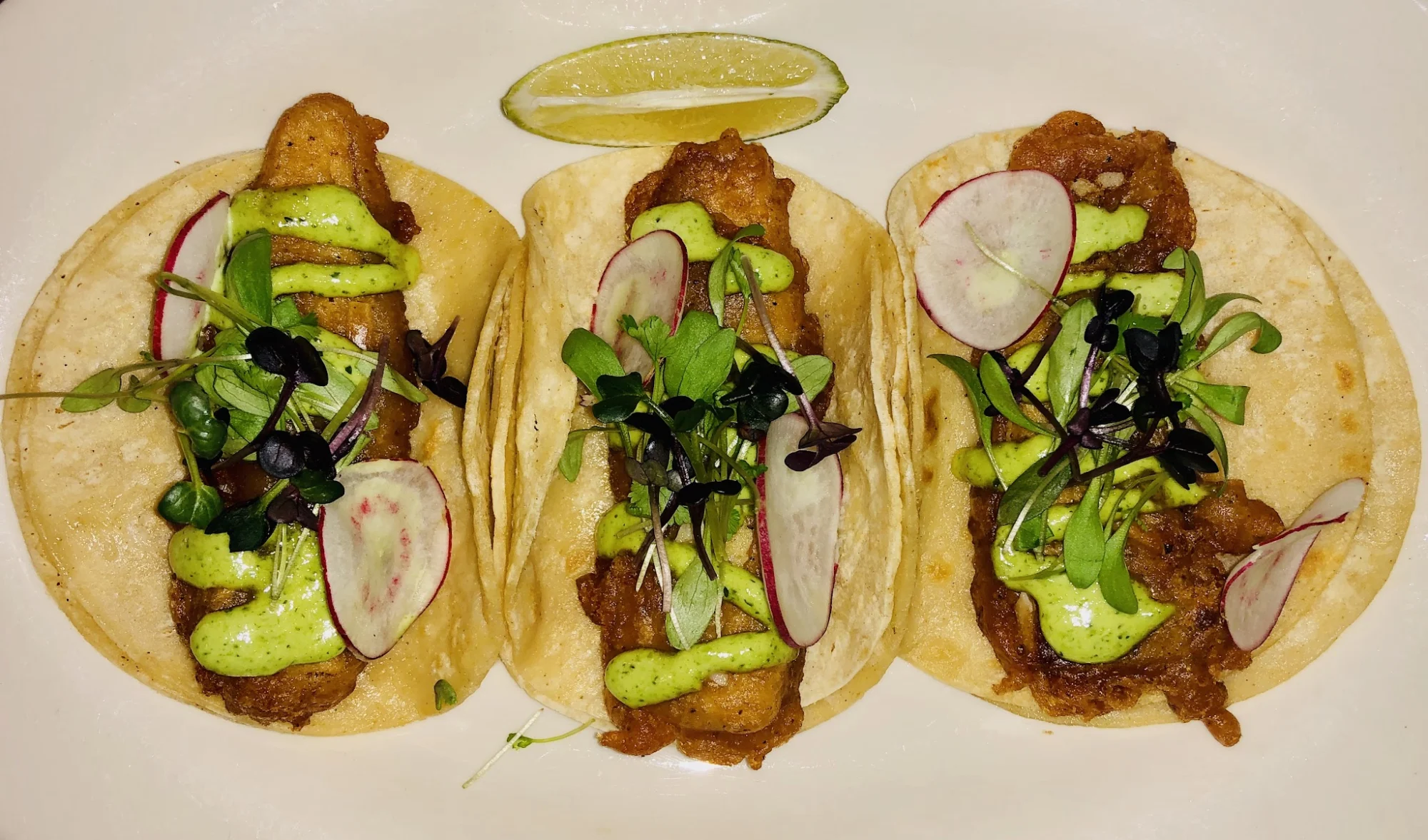 Three tacos with toppings on a plate at Taqueria Tlaxcalli, Parkchester.