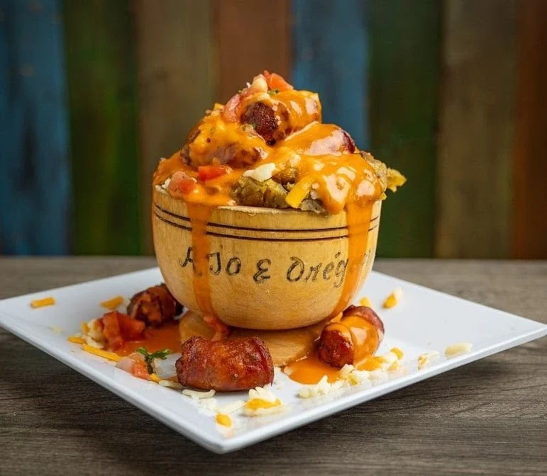 Decorative bowl with hearty dish topped with cheese, tomatoes, and sausages at Ajo y Oregano, Parkchester.