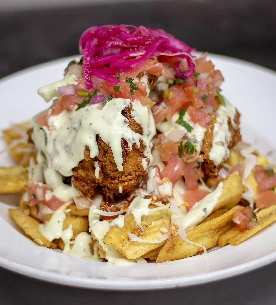 Plate of food with fried chicken, plantain chips, pink pickled onions, and toppings at Seis Vecinos, Mott Haven.