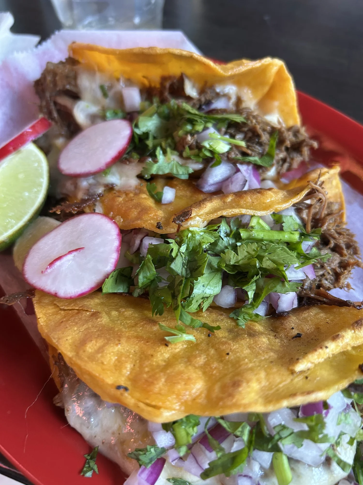 Close-up of three tacos with beef, radishes, lime, and cilantro on a red plate at Colima Taqueria, Belmont.