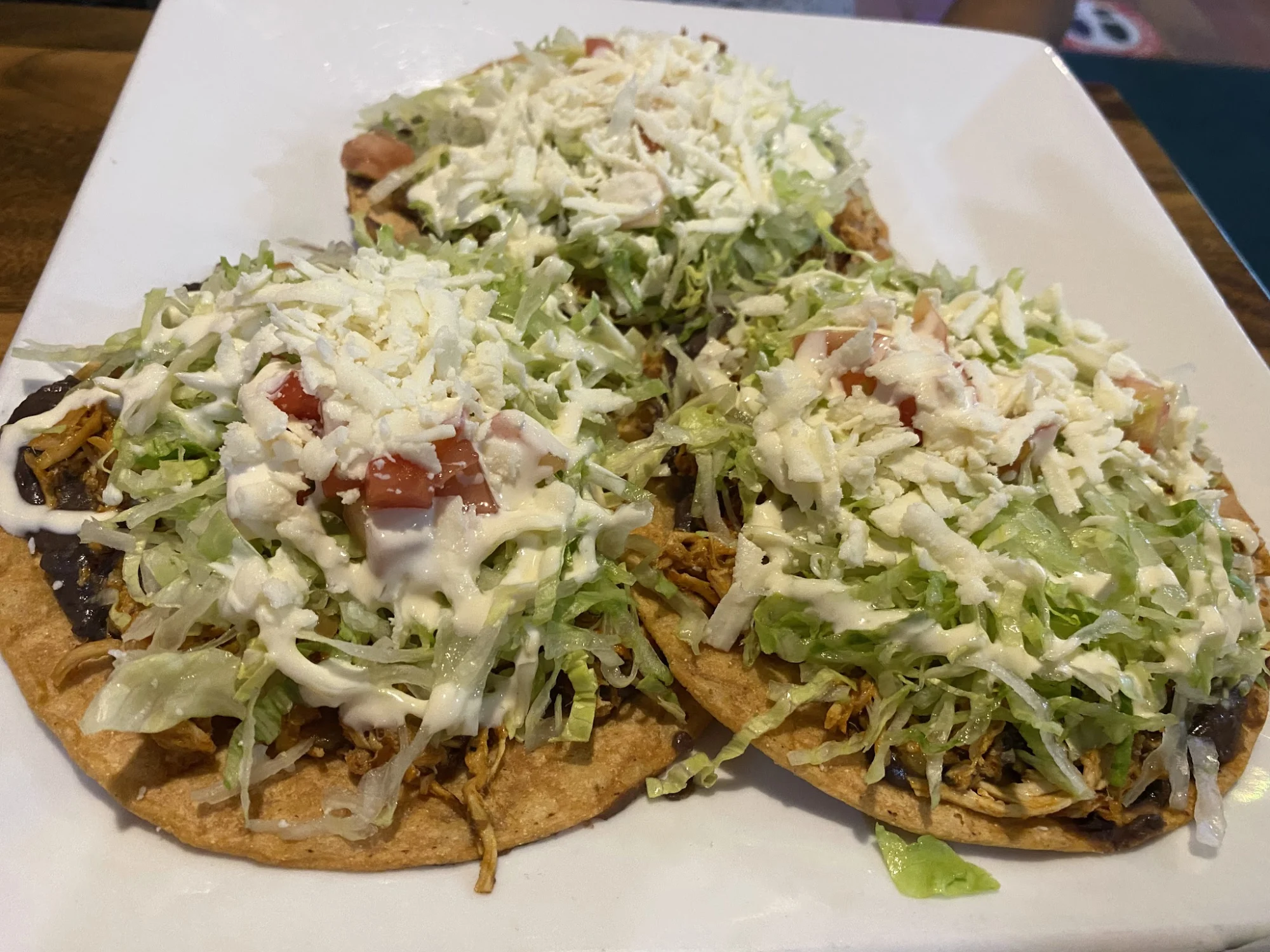 Estrellita Poblana 4 featured image Three tostadas topped with shredded lettuce, cheese, and tomato on a white plate at Estrellita Poblana 4, Pelham Bay.