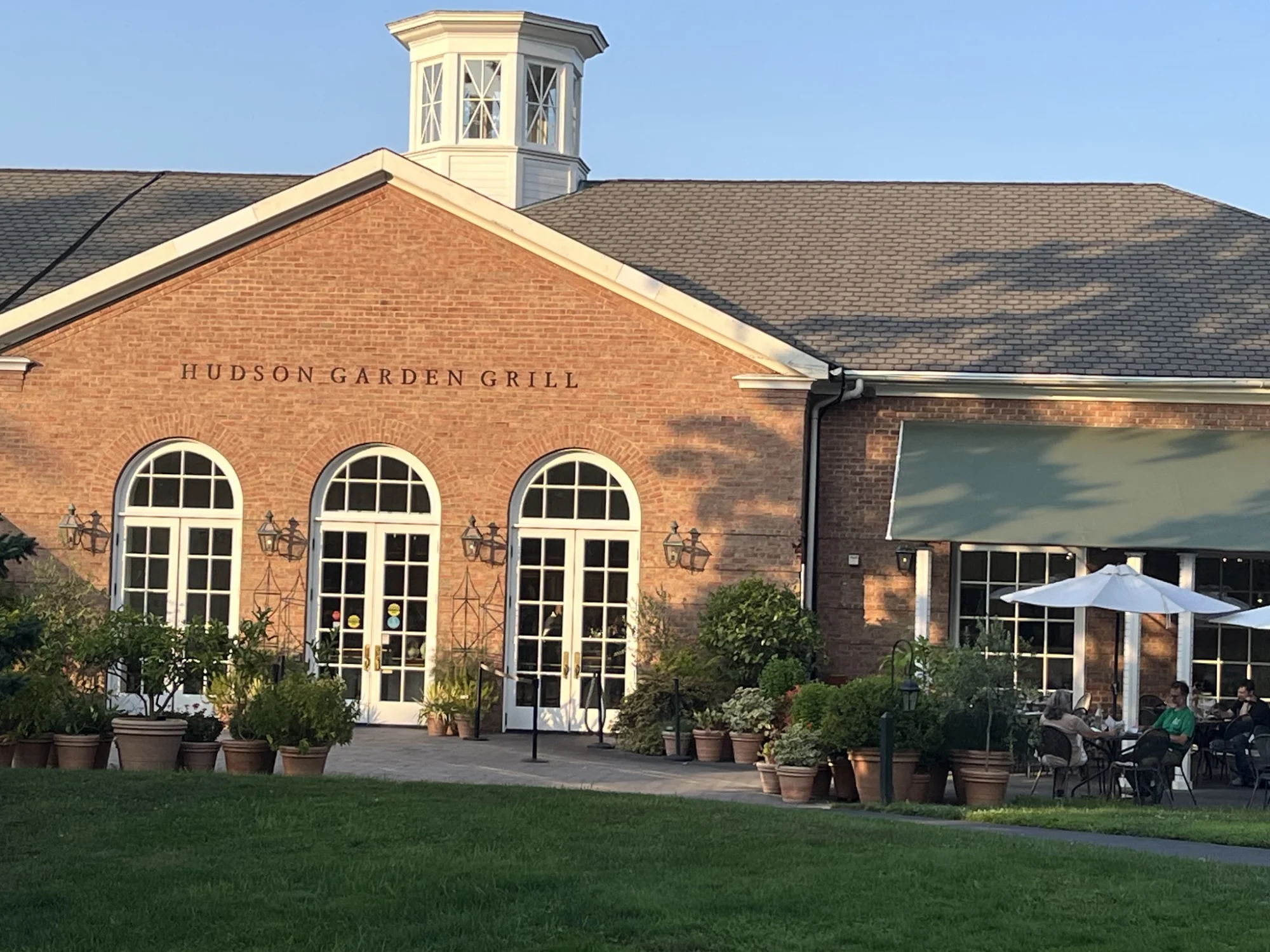 Exterior view of Hudson Garden Grill with large windows and green awning, Belmont, Bronx NYC.