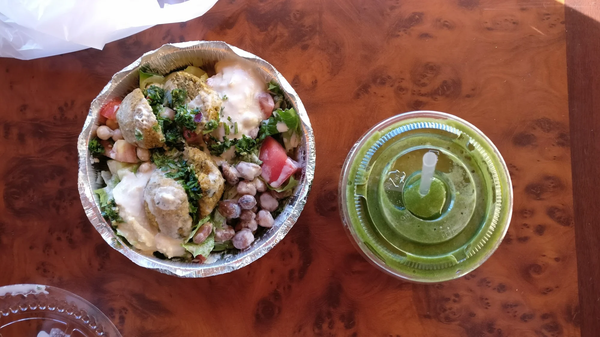 A falafel salad with greens, beans, and sauce next to a green smoothie on a wooden table at Noho Juice Bar, NoHo.