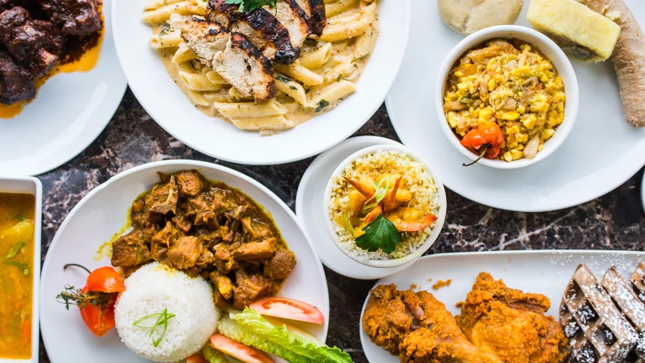 A variety of dishes with different meats, rice, and vegetables on white plates at Lash West Indian & American Cuisine, Norwood.