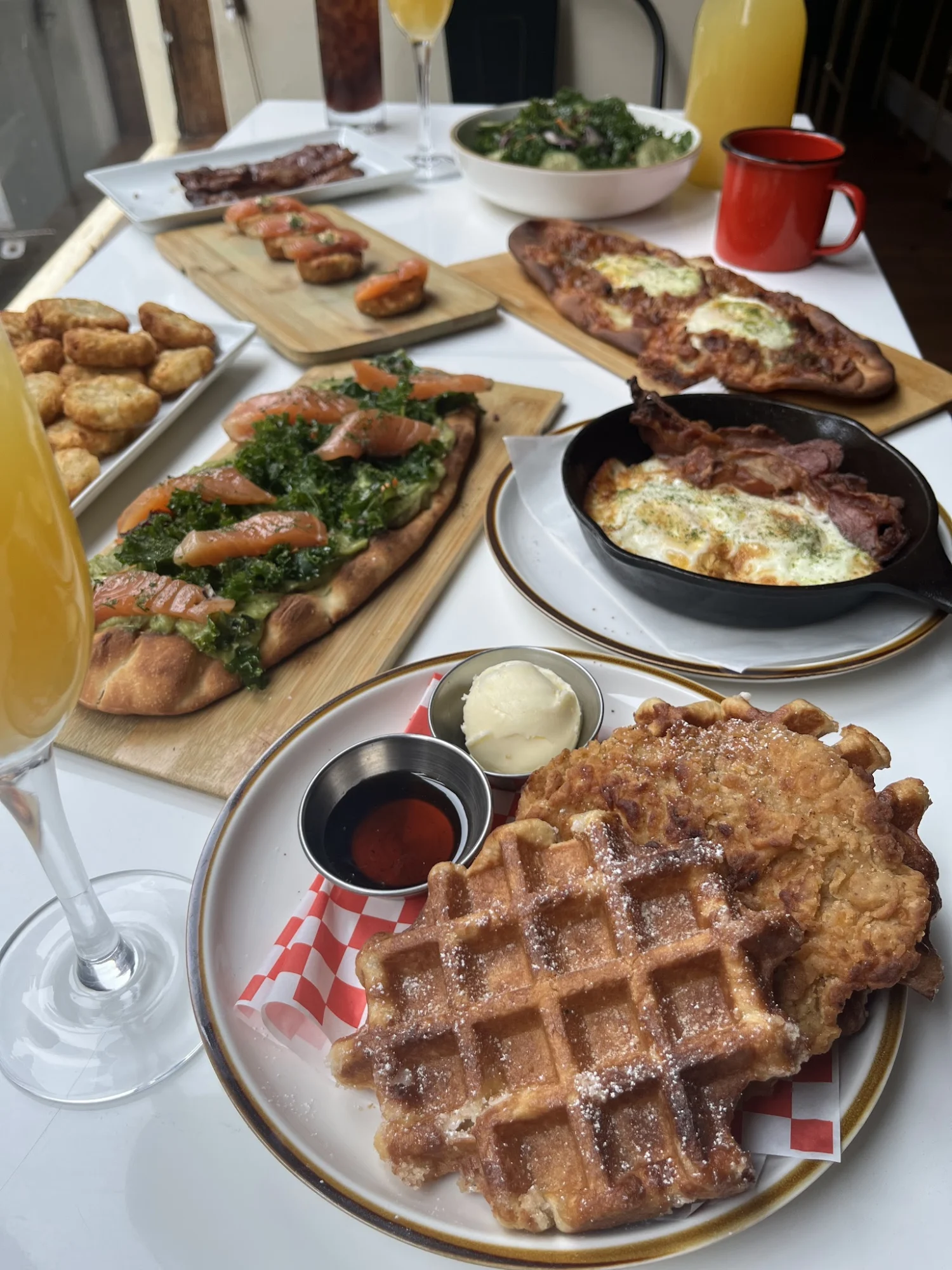 Variety of dishes including waffles, flatbreads, and drinks on a table at The Red Stache, Hell's Kitchen.