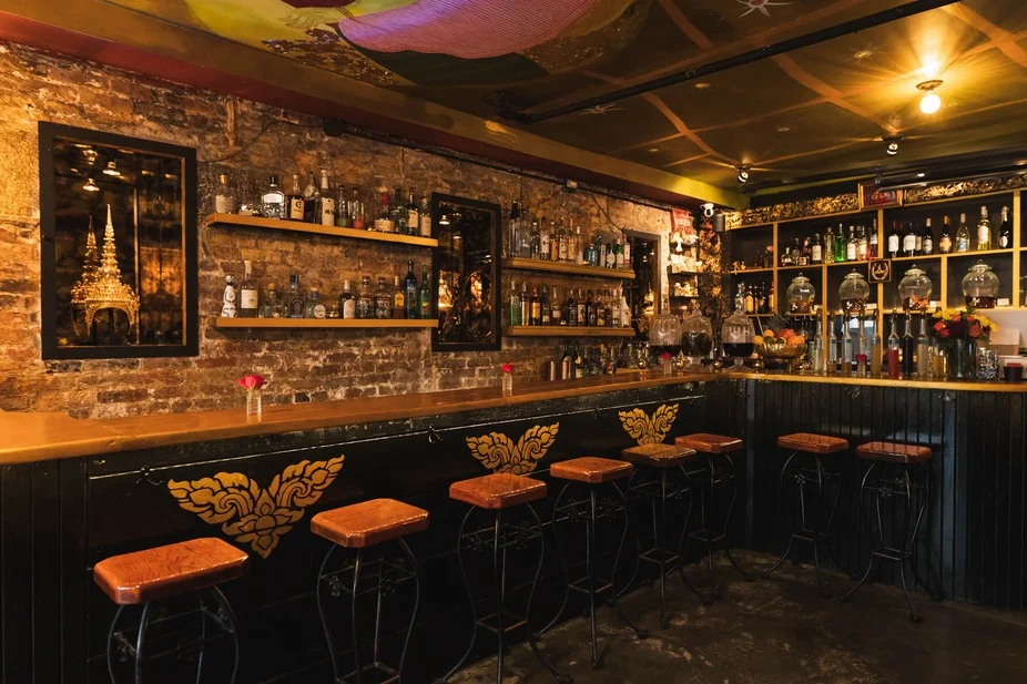 MayRee featured image Interior of MayRee showing a bar with stools, shelves with bottles, and decorative art in East Village, Bronx NYC.