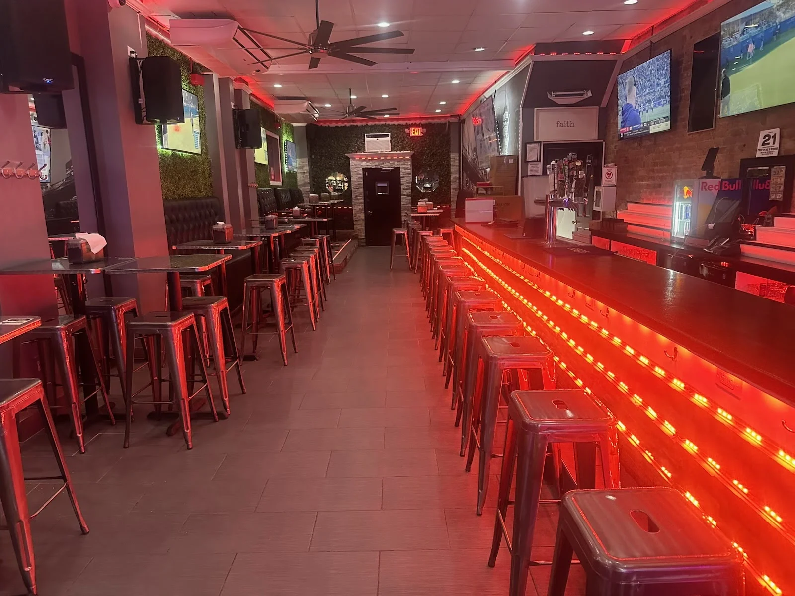 Interior of Social cafe101 with a long bar and stools, red lighting, and TV screens, Westchester Square.
