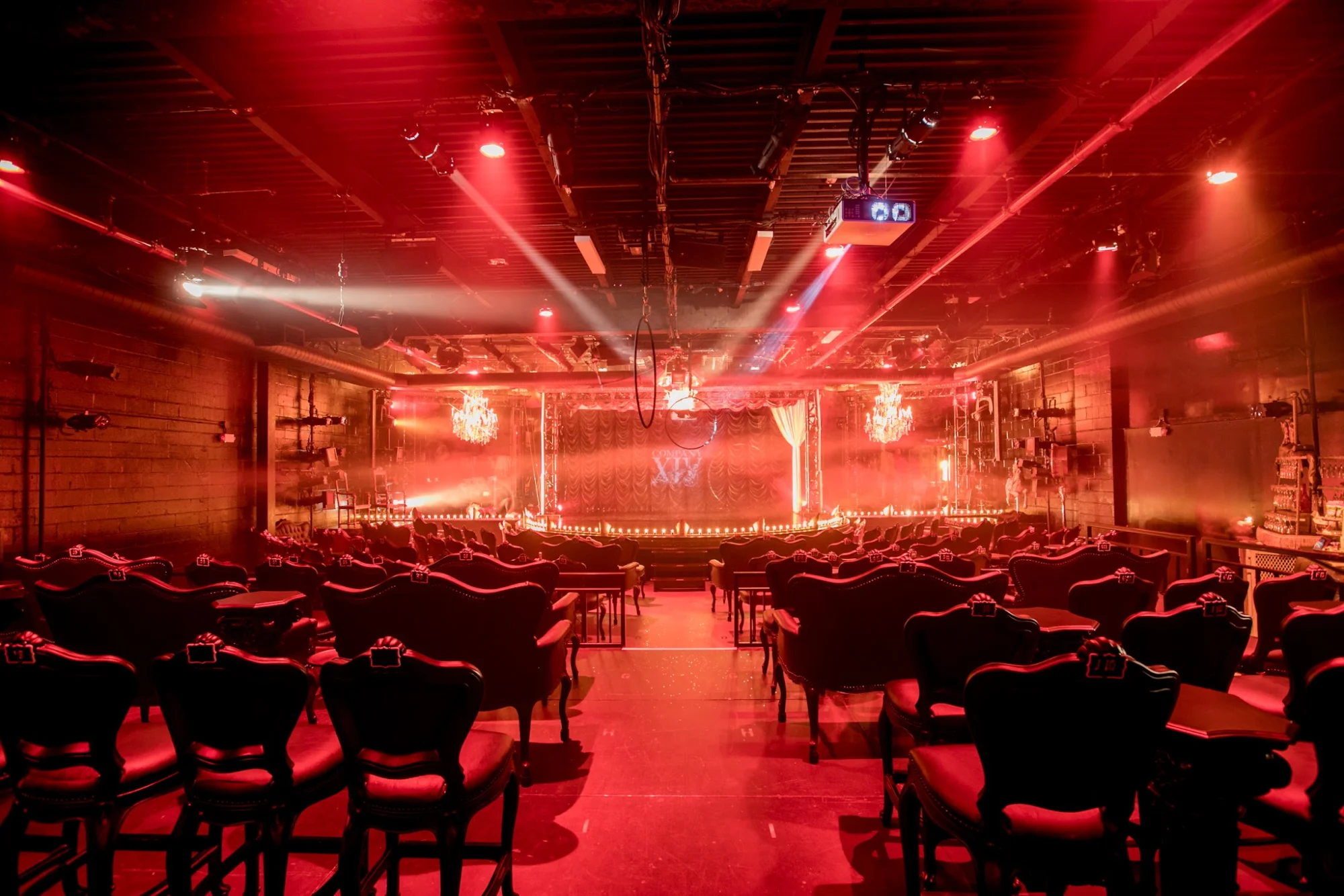 Théâtre XIV by Company XIV featured image Interior of Théâtre XIV with stage and chairs, dim red lighting, Bushwick.