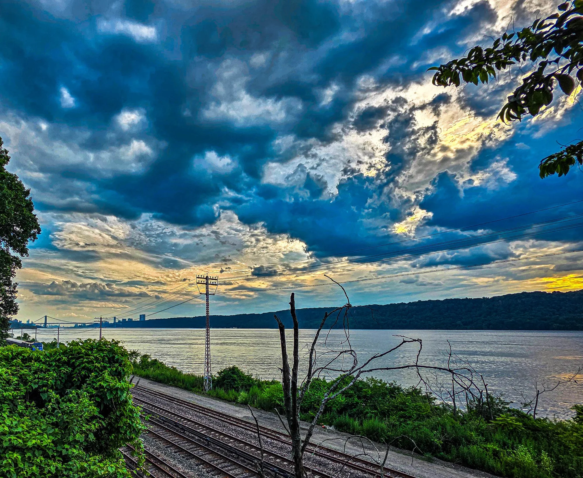 Dramatic cloudy sky over a river with a railway and lush greenery, Riverdale Park, Riverdale.