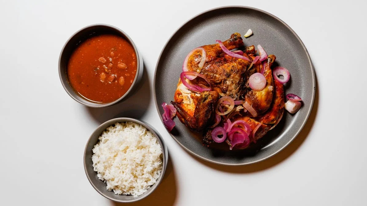 Plate with grilled chicken, red onions, rice, and beans at Casa De Mamá, Tremont Bronx.
