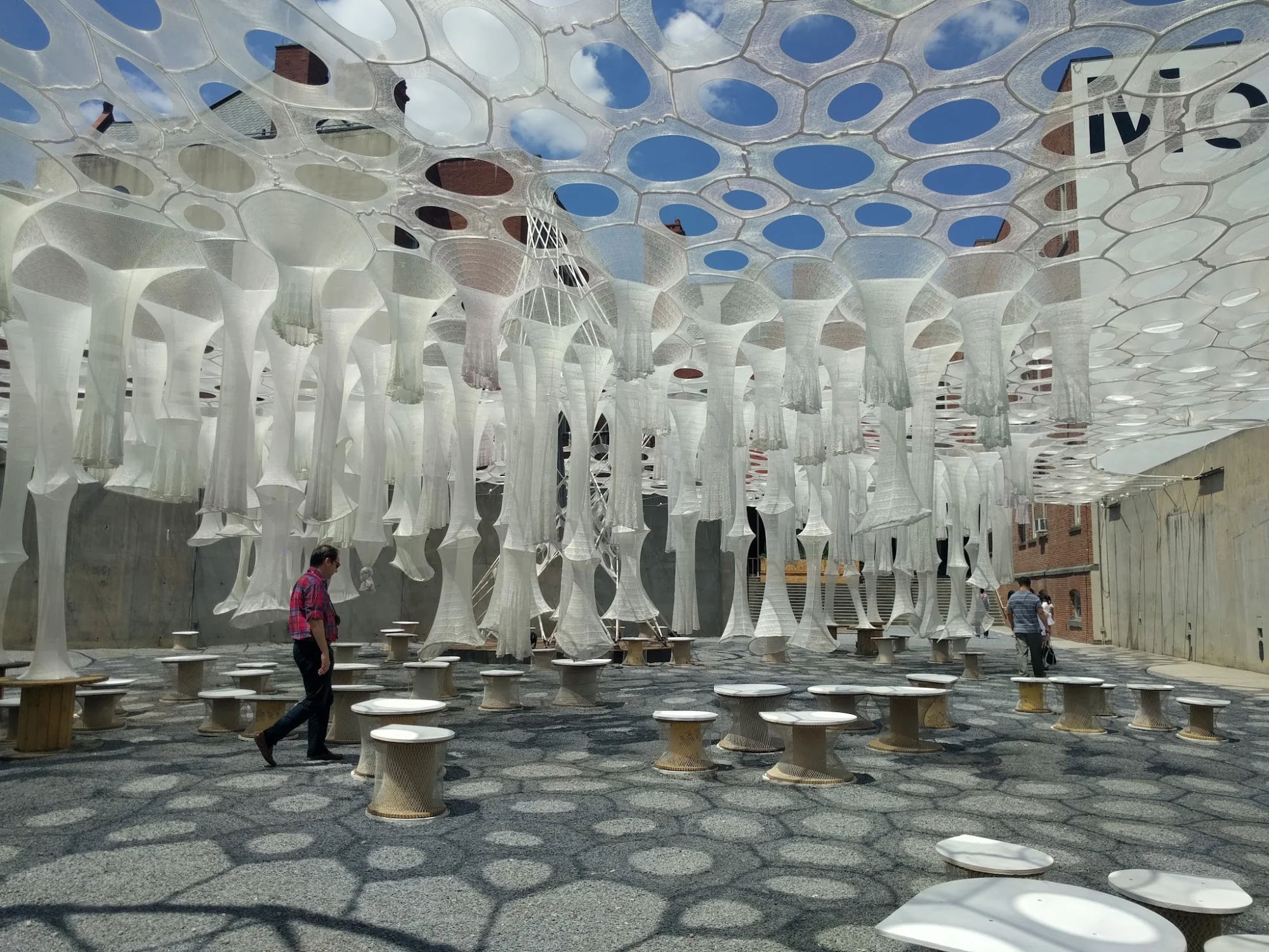 Outdoor art installation at MoMA PS1 in Long Island City, featuring hanging geometric structures and circular seating.