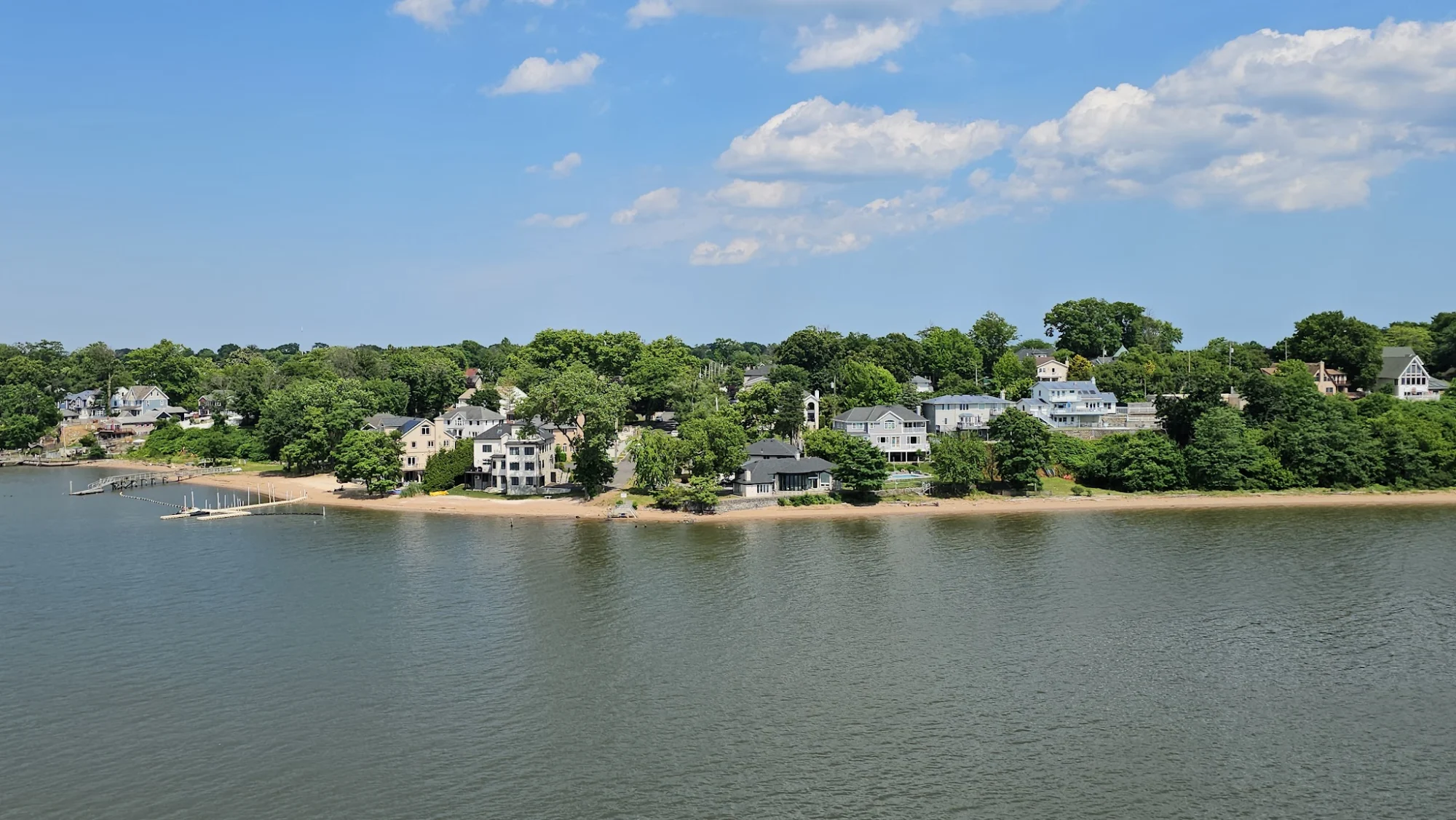A wide view of the shoreline with houses and trees along the water in Tottenville, Bronx NYC.