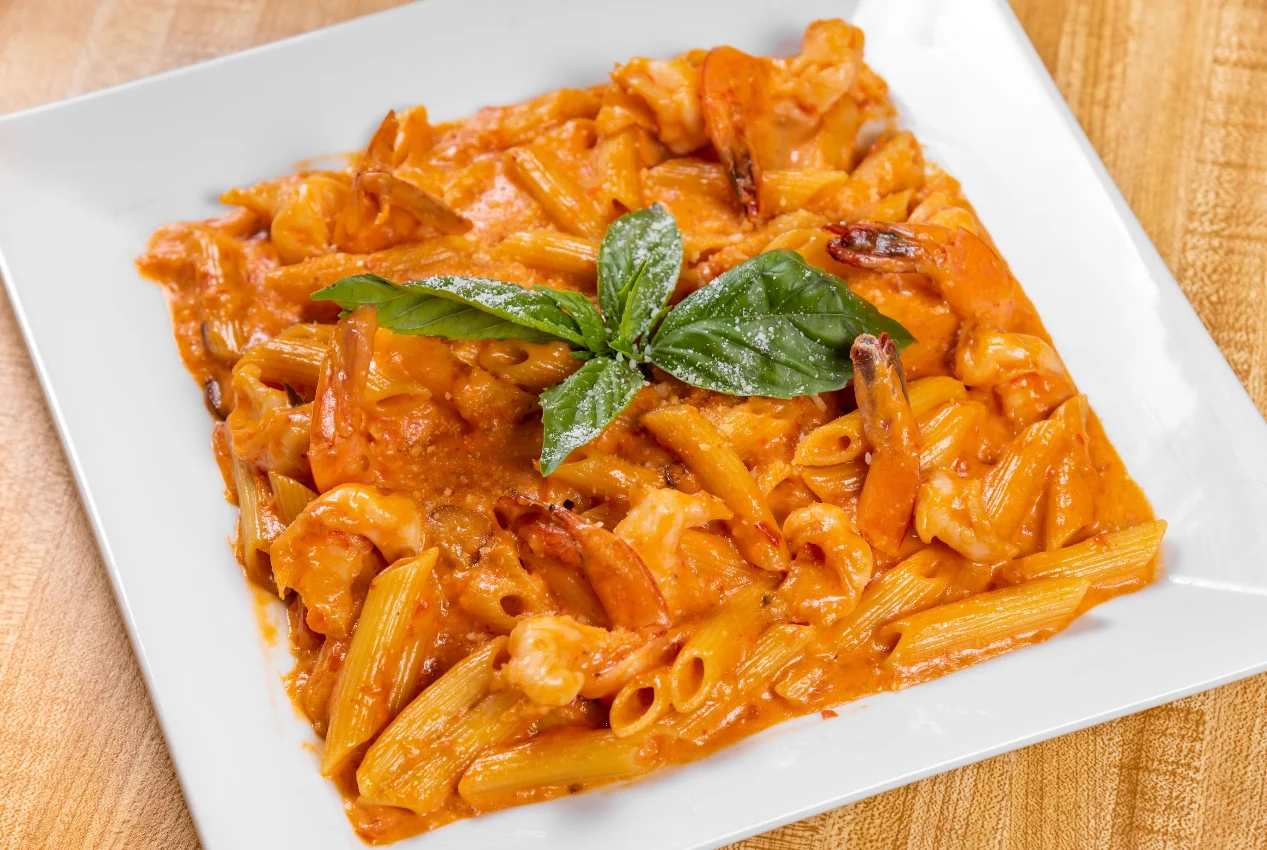 Famosa Pizza featured image Plate of pasta with shrimp and basil on a wooden table at Famosa Pizza, Belmont Bronx NYC.