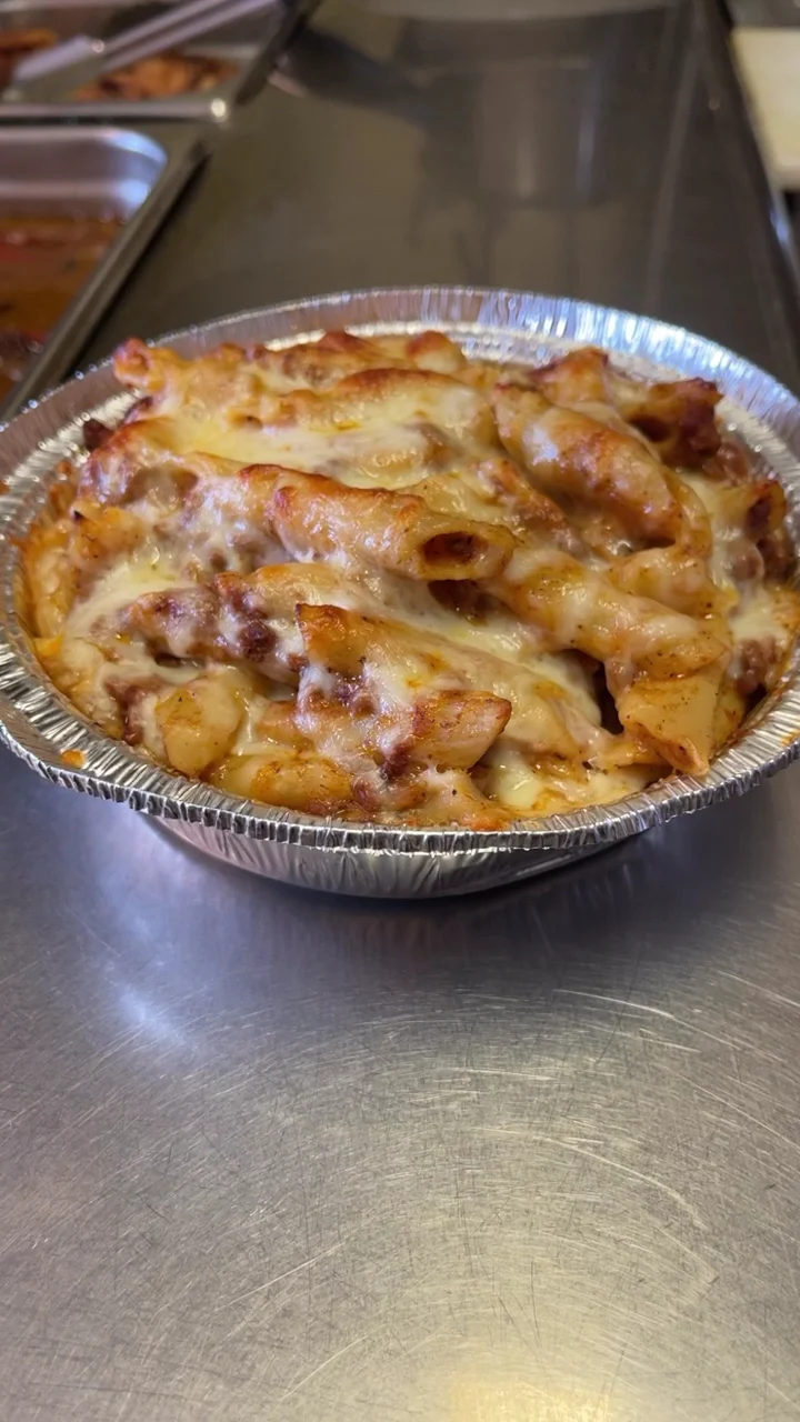 Baked pasta in a foil container on a metal surface at La Reina Restaurant, Throgs Neck.