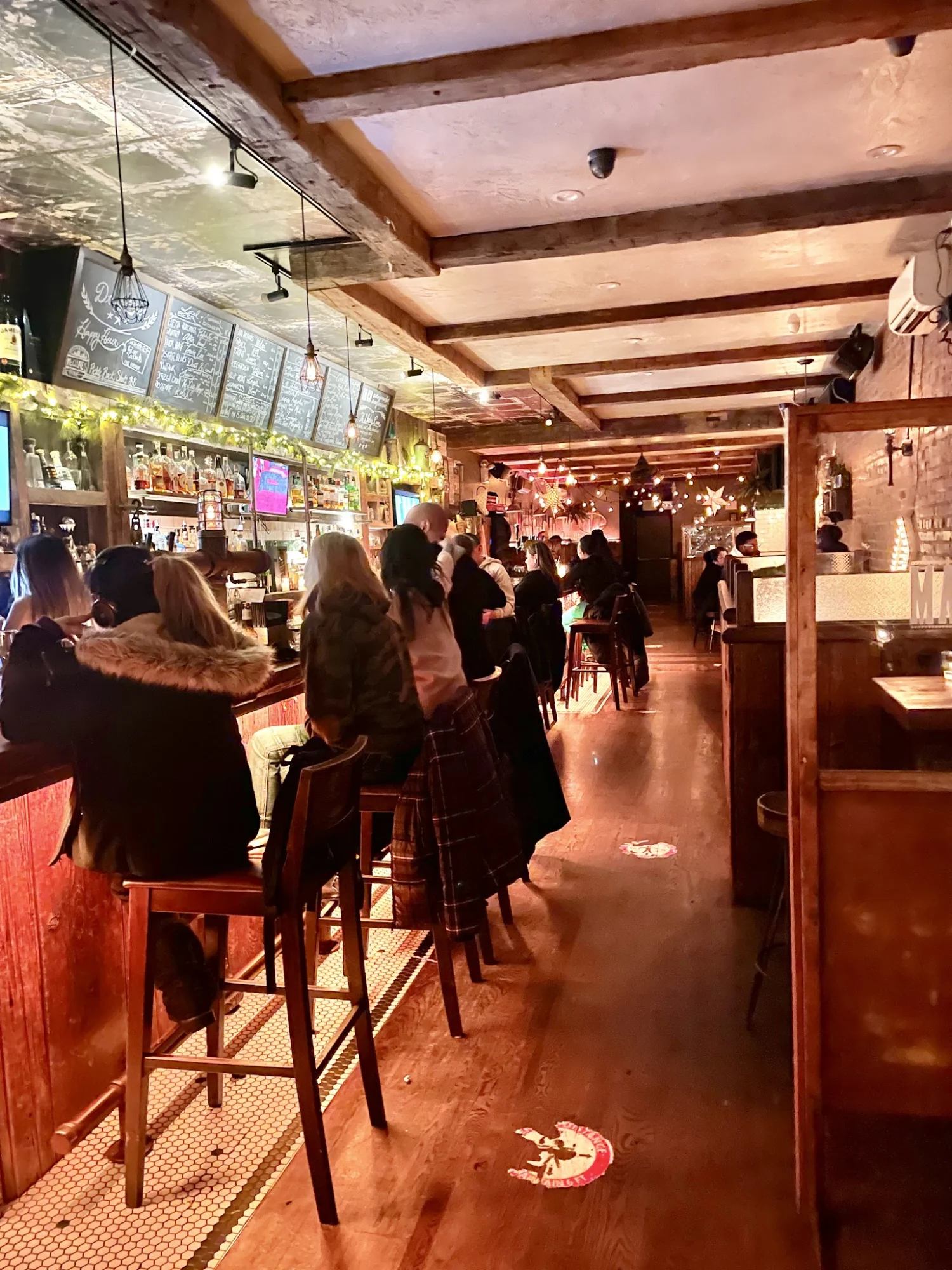 Interior of Maggie Mae's Bar in Sunnyside, Bronx with a long bar and patrons seated on stools.