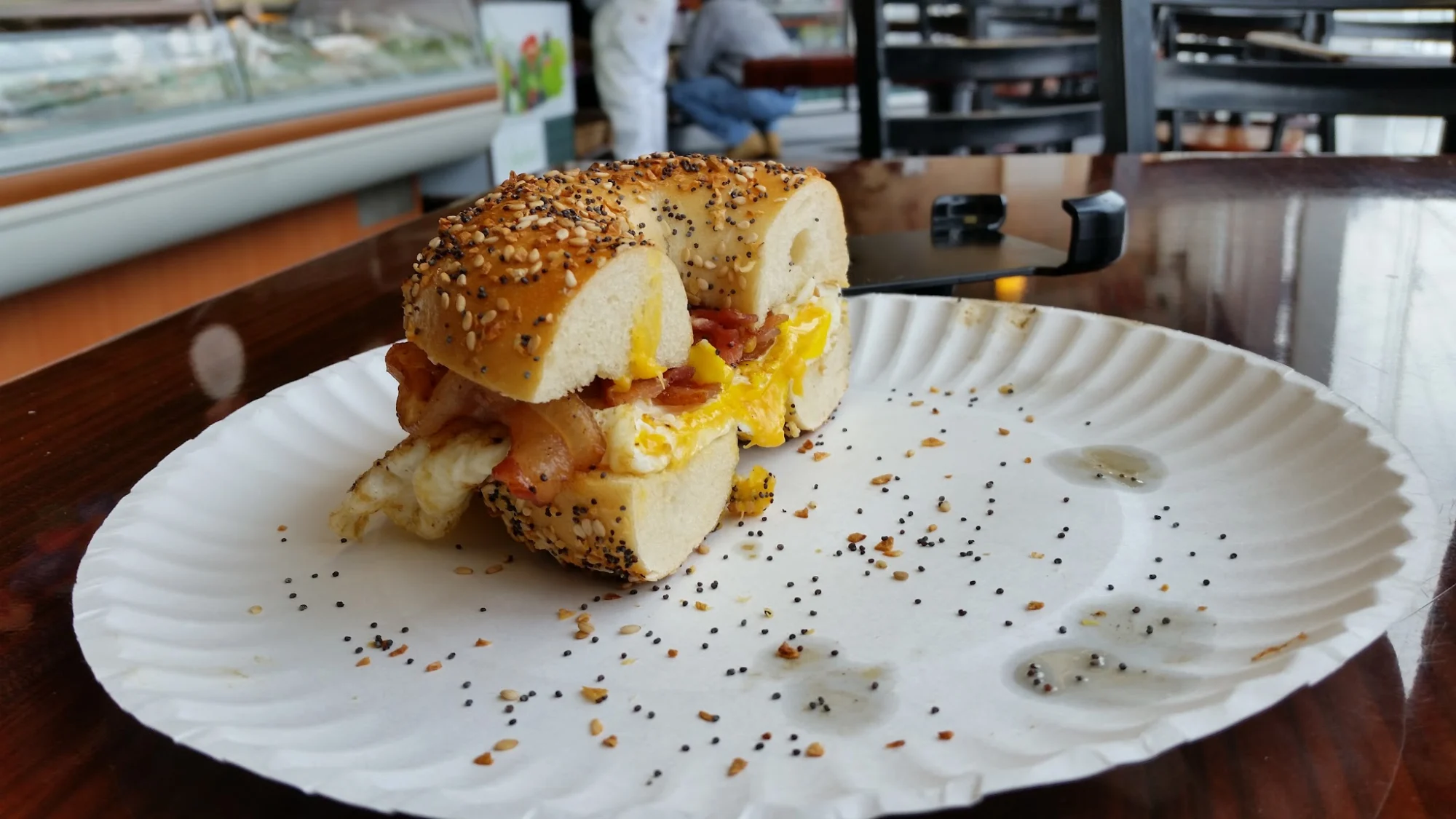 Traditional Bagel Cafe featured image Everything bagel sandwich with bacon, egg, and cheese on a paper plate, Traditional Bagel Cafe, Bronx NYC.