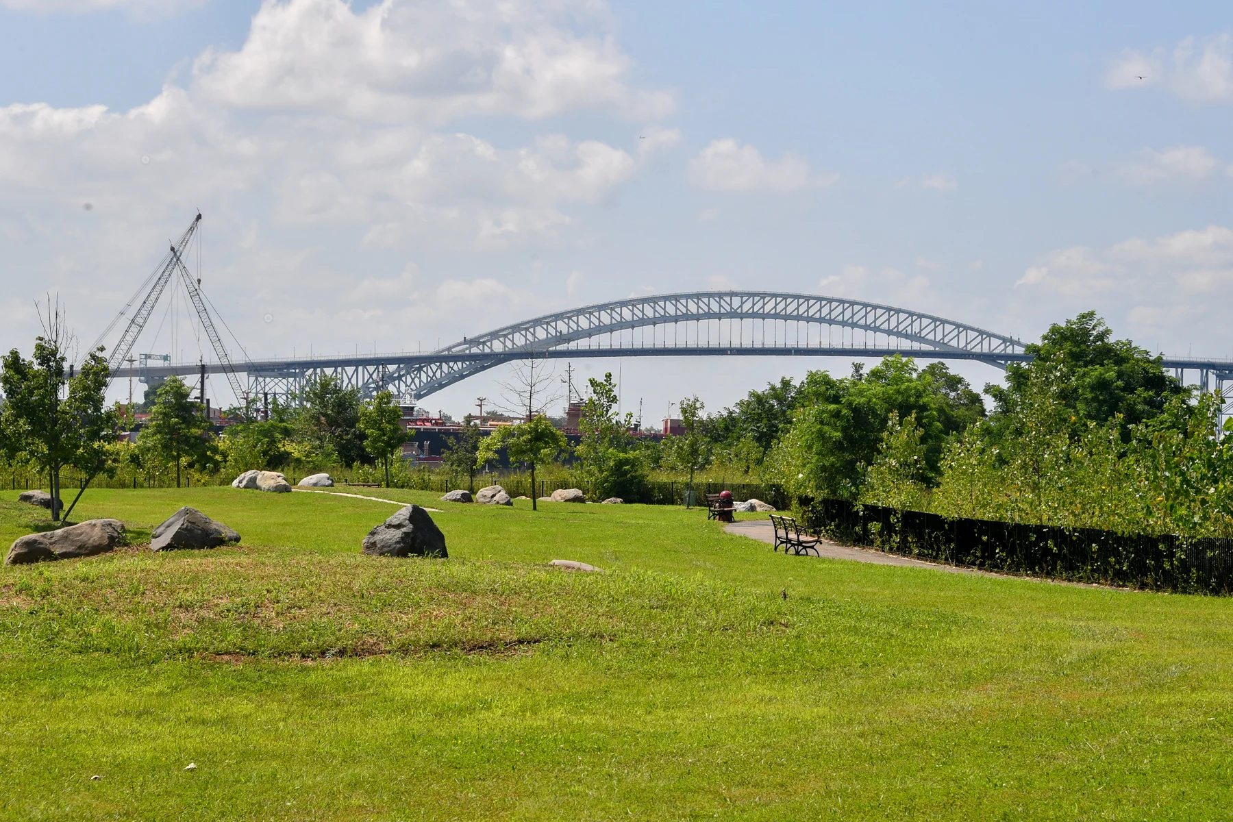 Wide grassy area with a view of a large bridge and a crane in Heritage Park, West New Brighton.