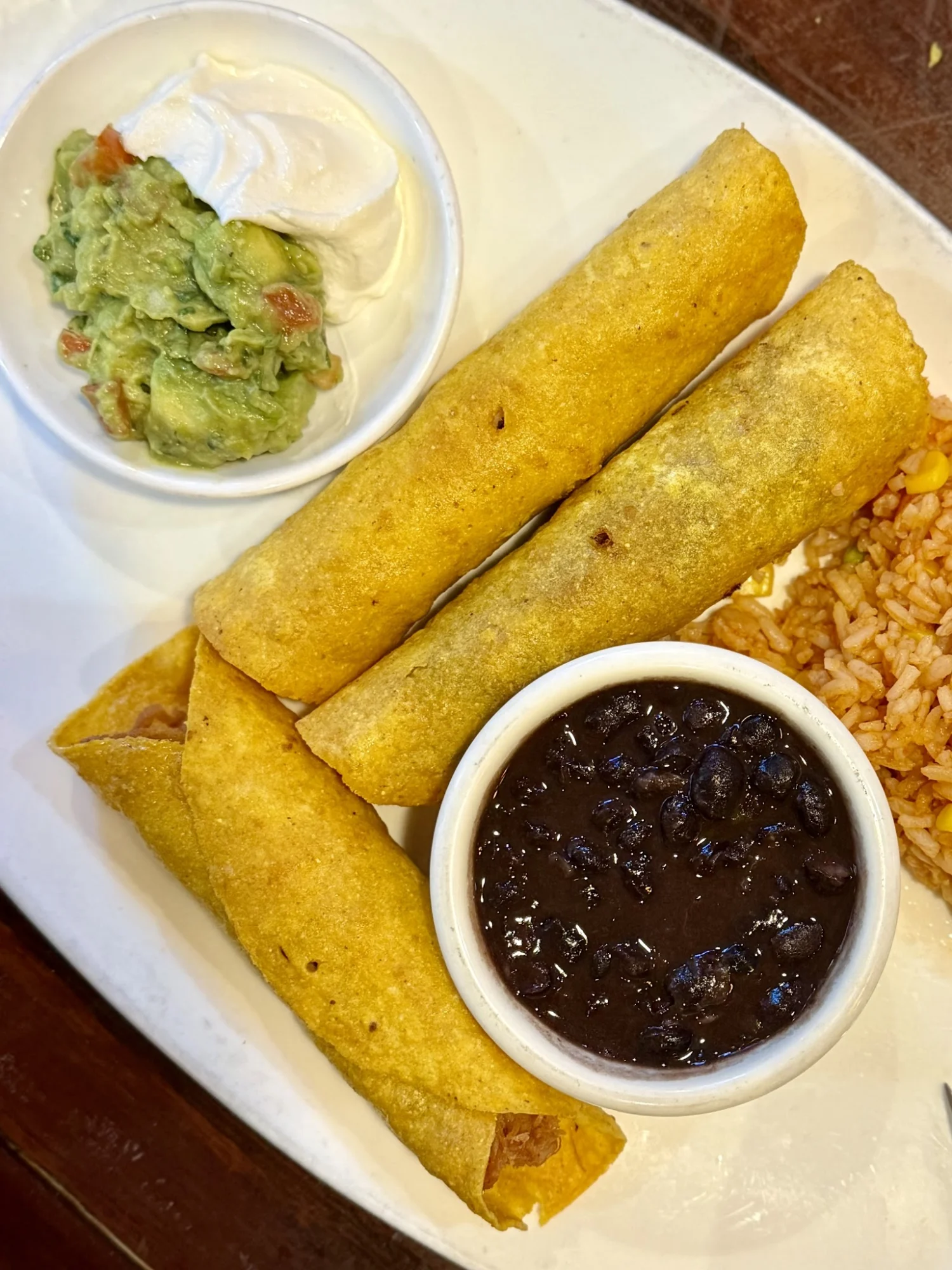 Three crispy tortilla rolls with sides of black beans, guacamole, and sour cream at Mamasita Bar & Grill, Hell's Kitchen.