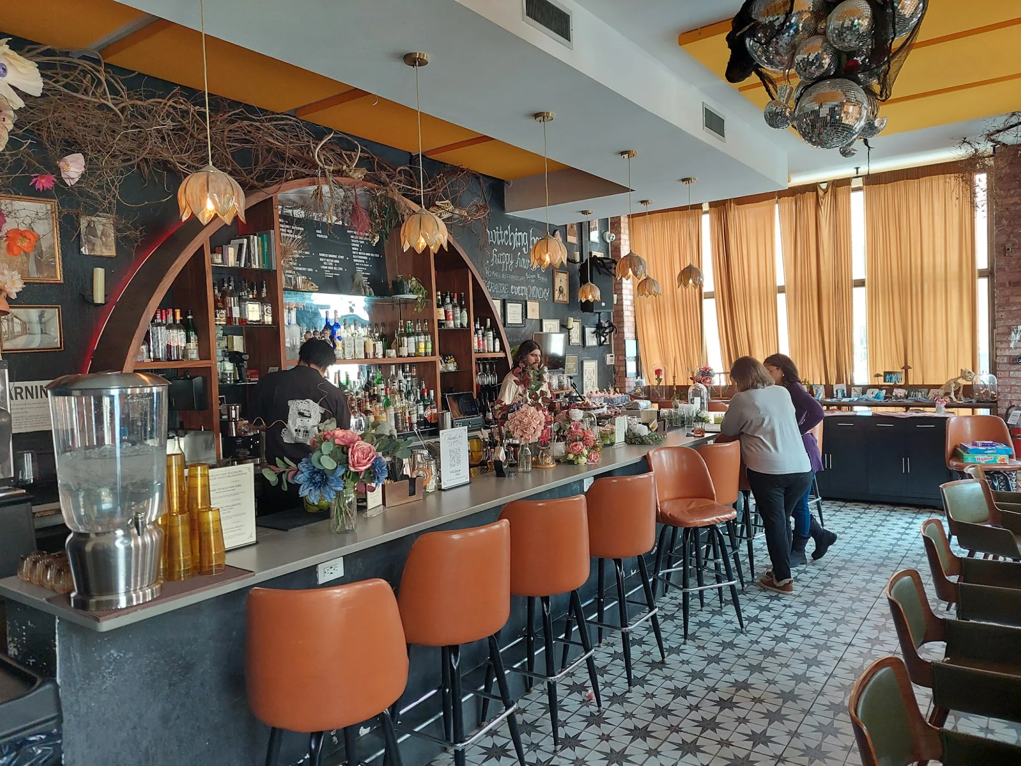 Witching Hour featured image Interior of Witching Hour, Bushwick, with a bar, orange stools, and decorative lights.