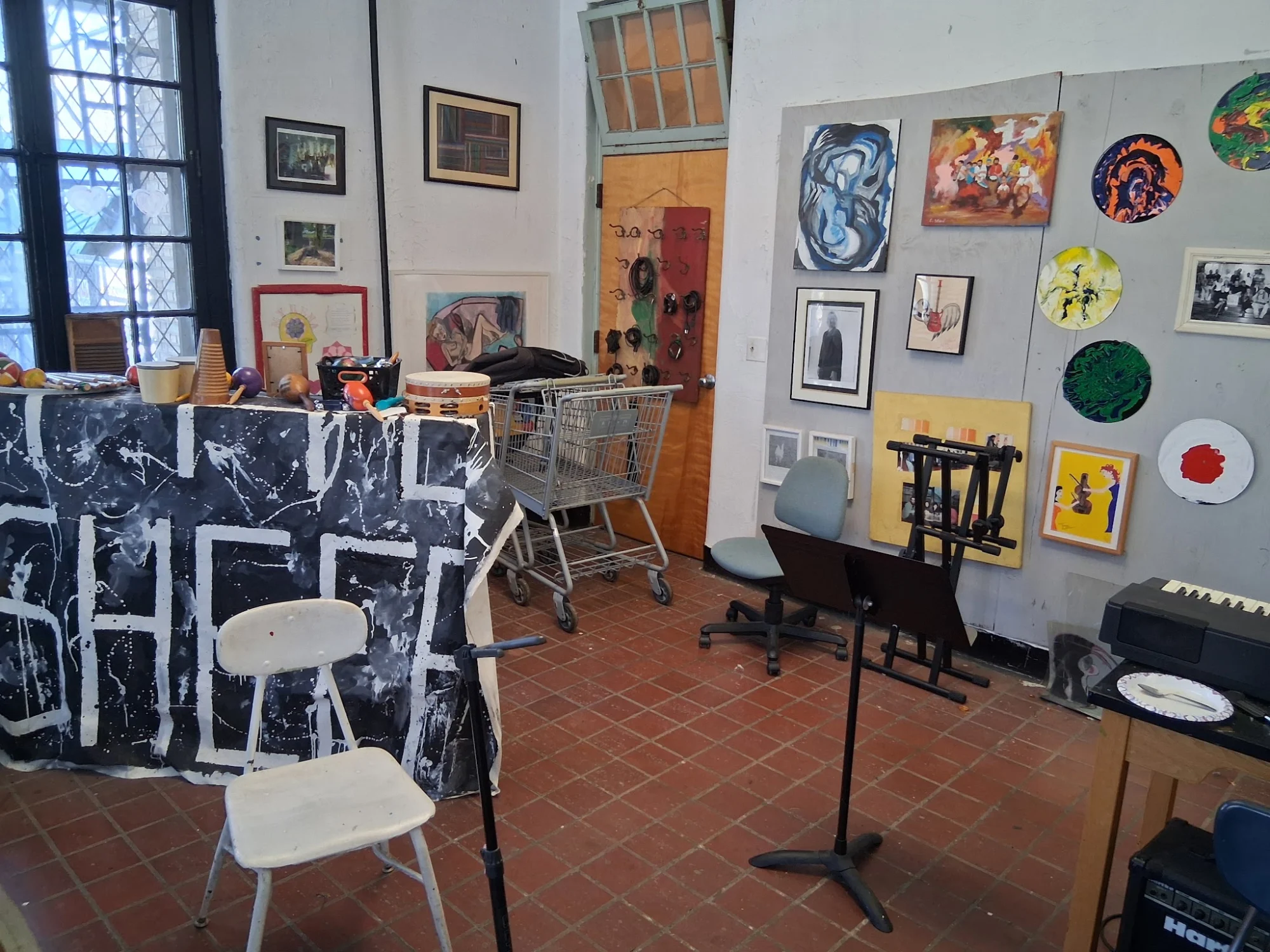 Interior of The Living Museum, Bellerose, Bronx NYC with artwork displays on the walls and a shopping cart against a brick floor.