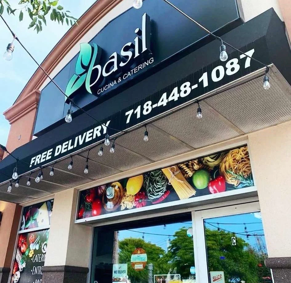 Exterior of Basil Cucina & Catering in Mariners Harbor with signage and delivery information.
