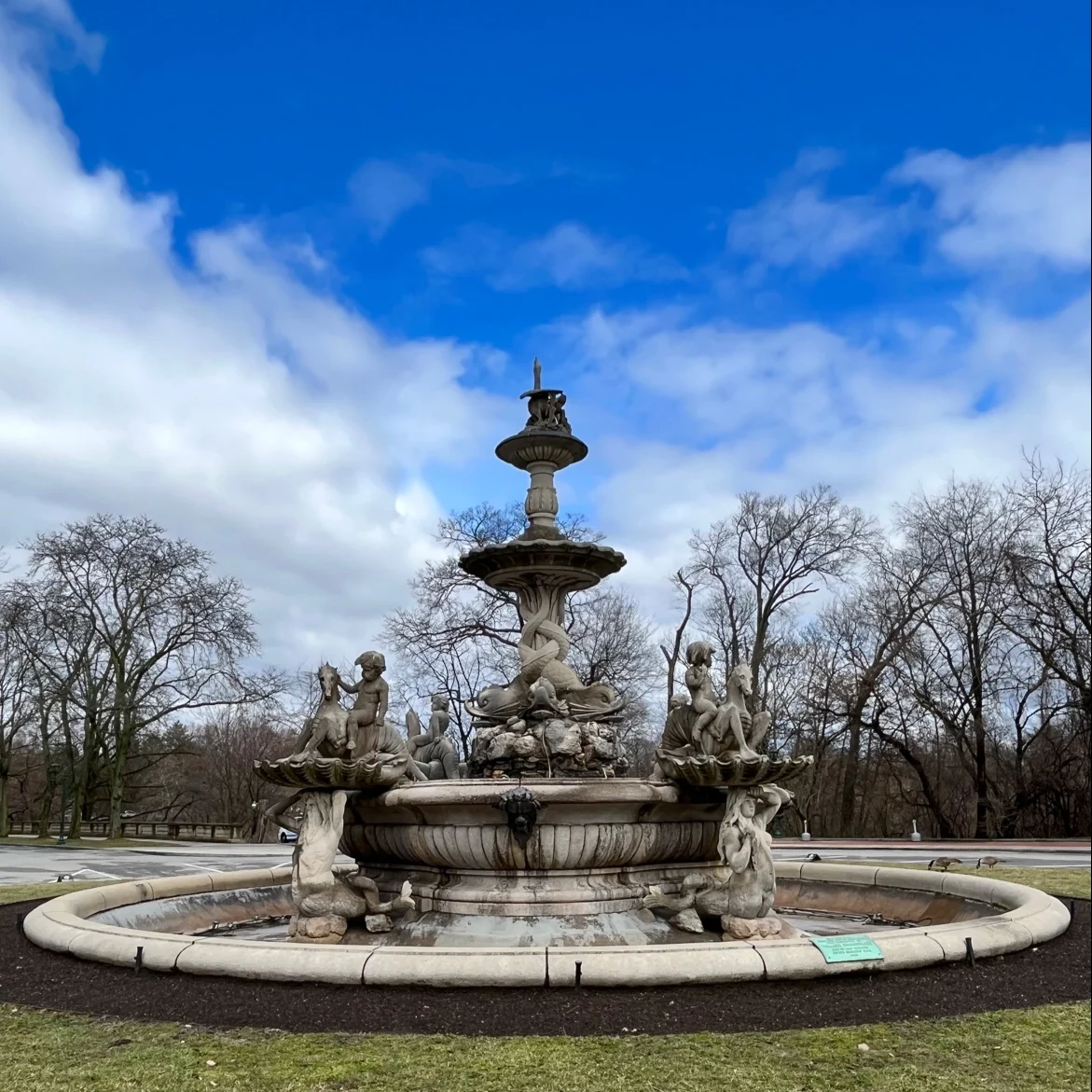 Rockefeller Fountain in Belmont, Bronx with ornate sculptures and a blue sky backdrop.