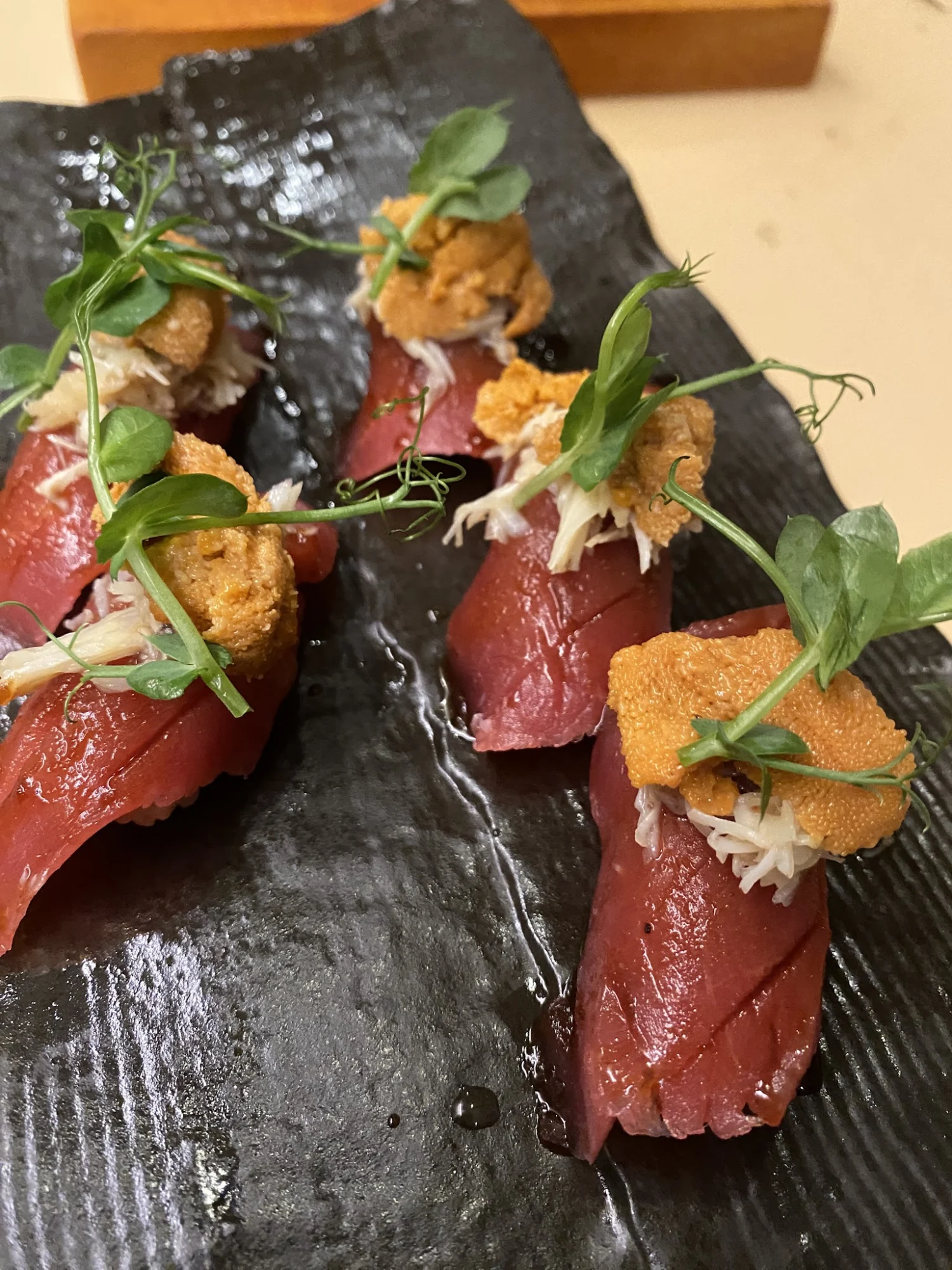 Domo omakase featured image Close-up of nigiri topped with uni and herbs on a dark plate at Domo Omakase, NoMad.