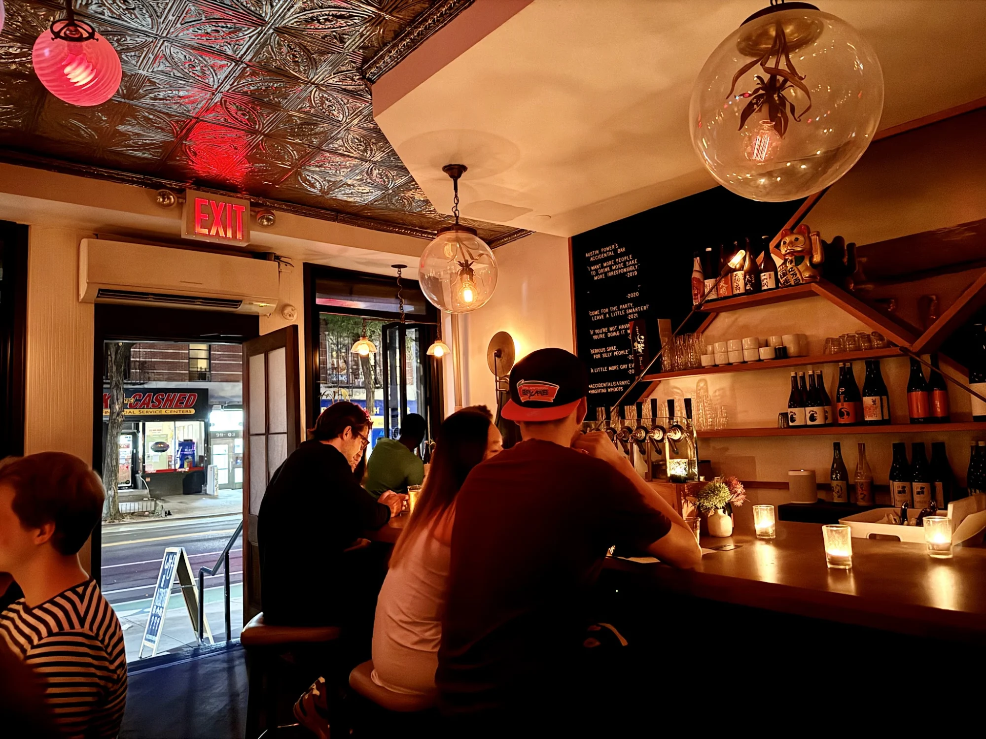 Interior of Accidental Bar, East Village. Cozy bar area with patrons and warm lighting.