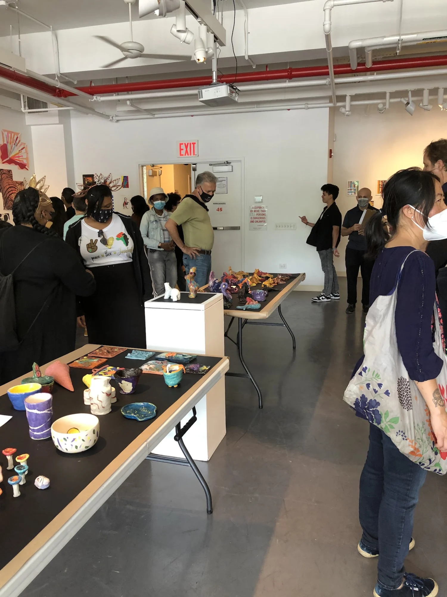 Interior view of Bronx River Art Center, West Farms, Bronx, with people viewing art on tables.