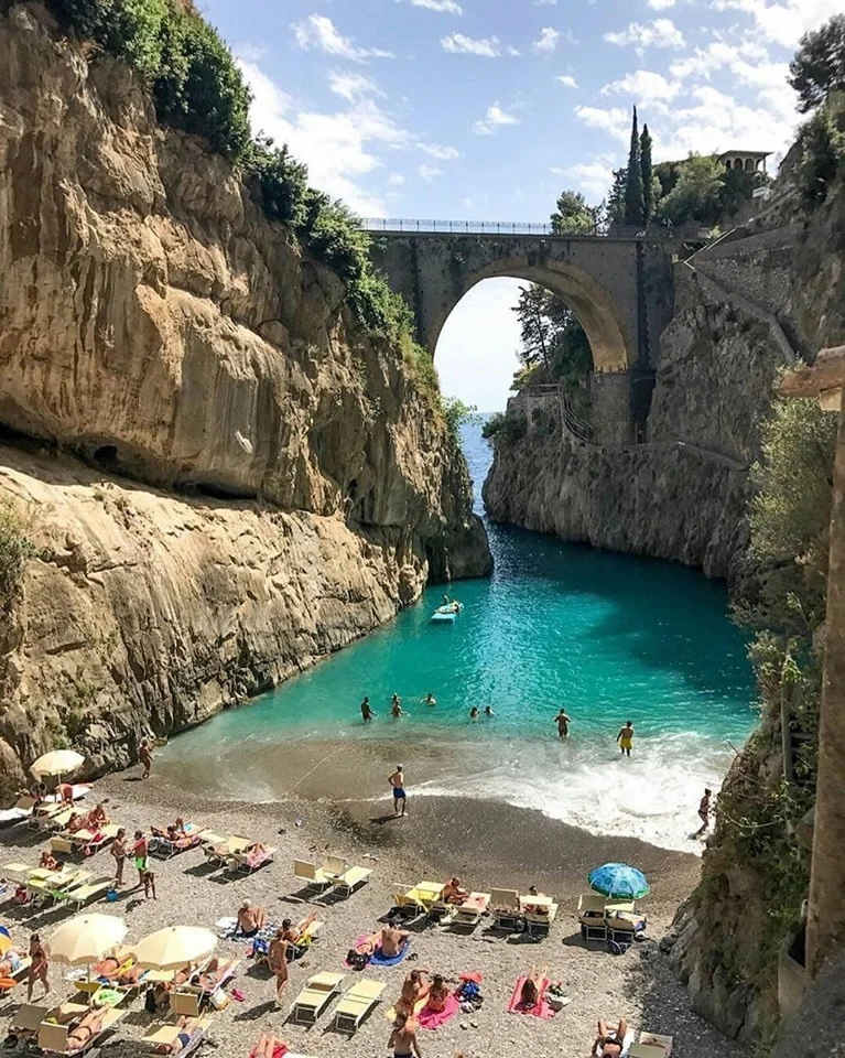 Anemos Tours featured image Beach in a rocky cove with sunbathers and an arched bridge in Astoria, Bronx NYC.