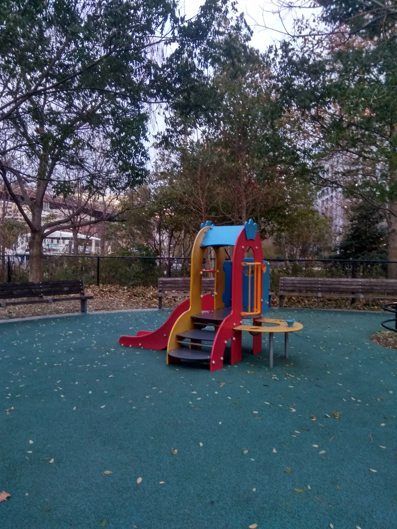 Colorful playground equipment in Pier 1 Playground, surrounded by trees in Brooklyn Heights.