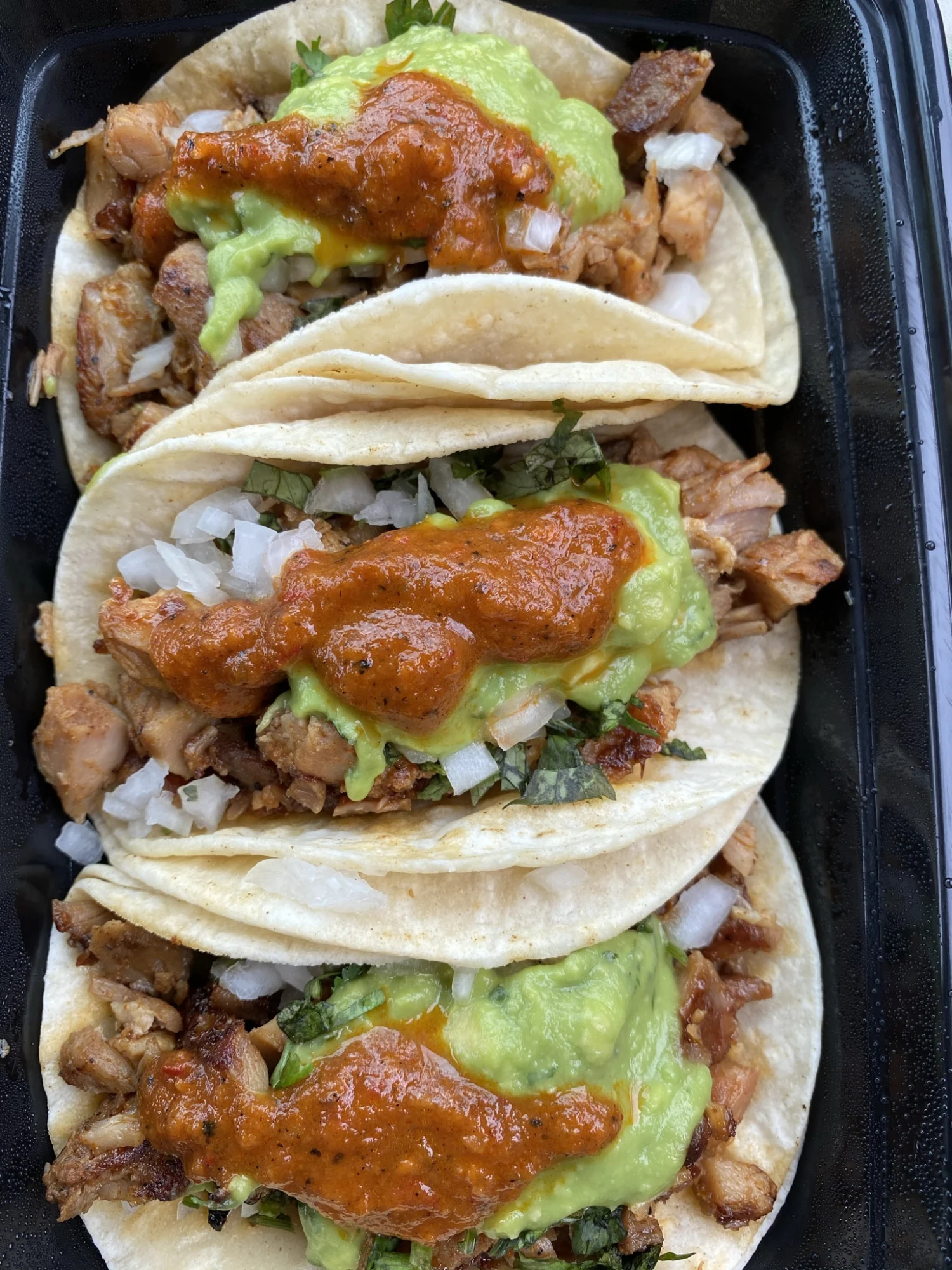 Three tacos filled with chicken, guacamole, chopped onions, and topped with red sauce in Fogon, Lincoln Square.