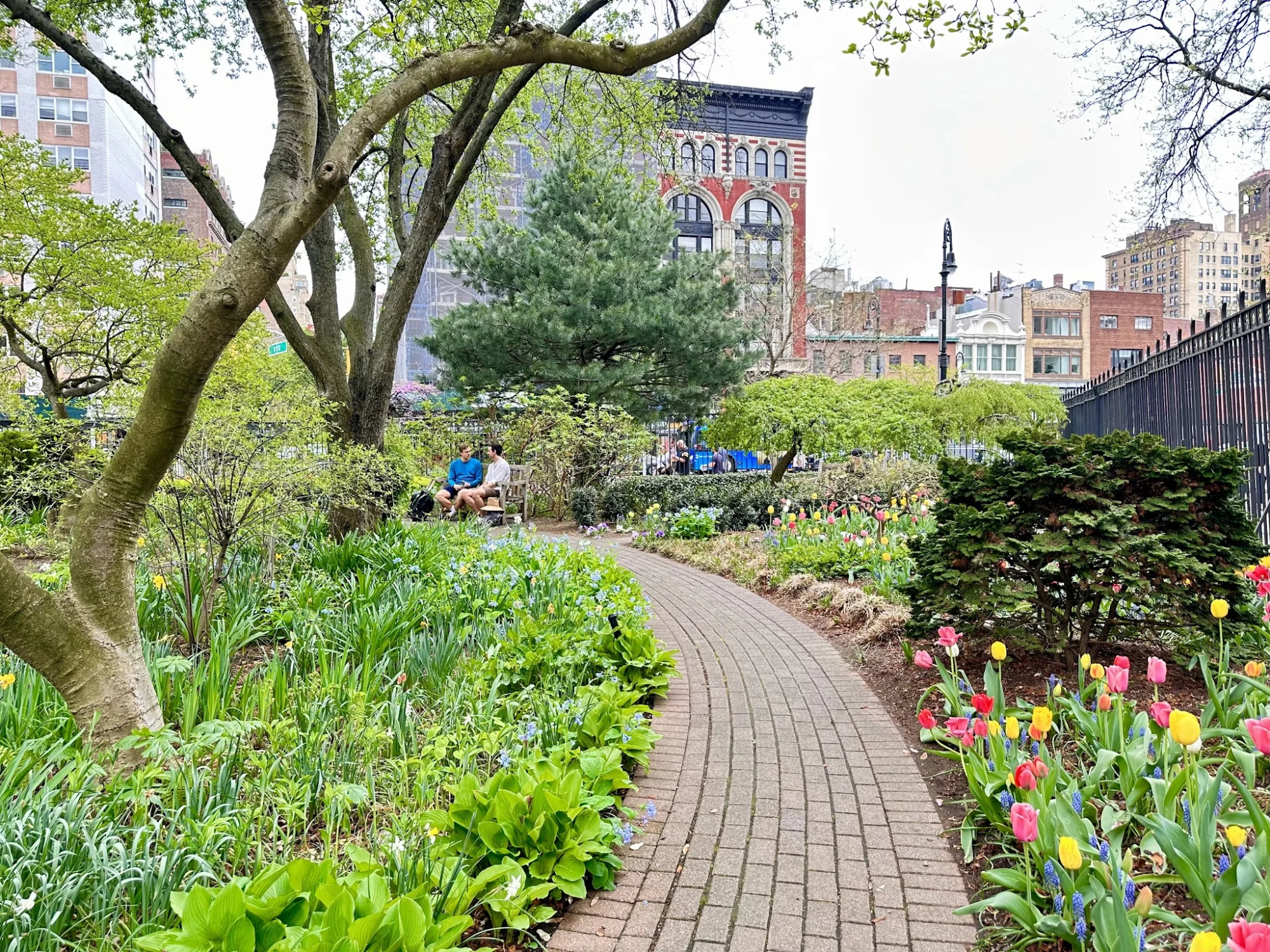 Brick path through Jefferson Market Garden with flowers and trees in Greenwich Village.