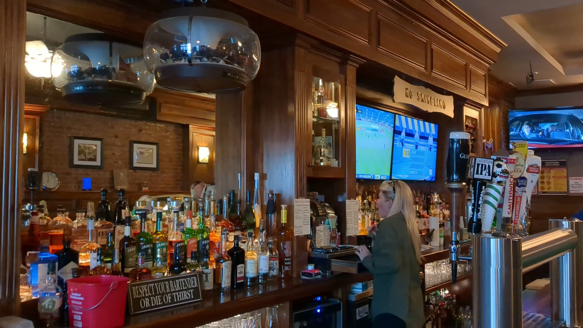 Rogers featured image Bar interior at Rogers, Rockaway Park with wooden bar, bottles, and TV screens.