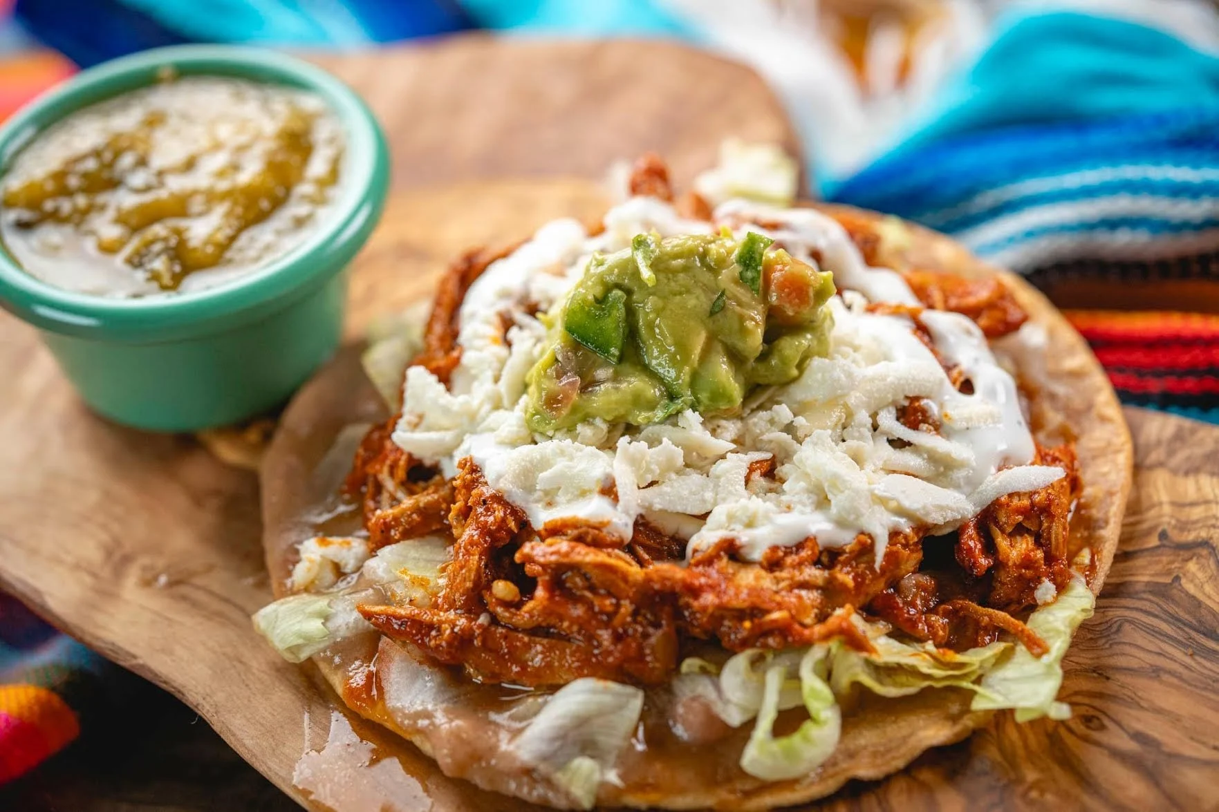 Tostada with shredded meat, cheese, guacamole, and a side of green sauce at Rinconcito Domex in Bedford-Stuyvesant.