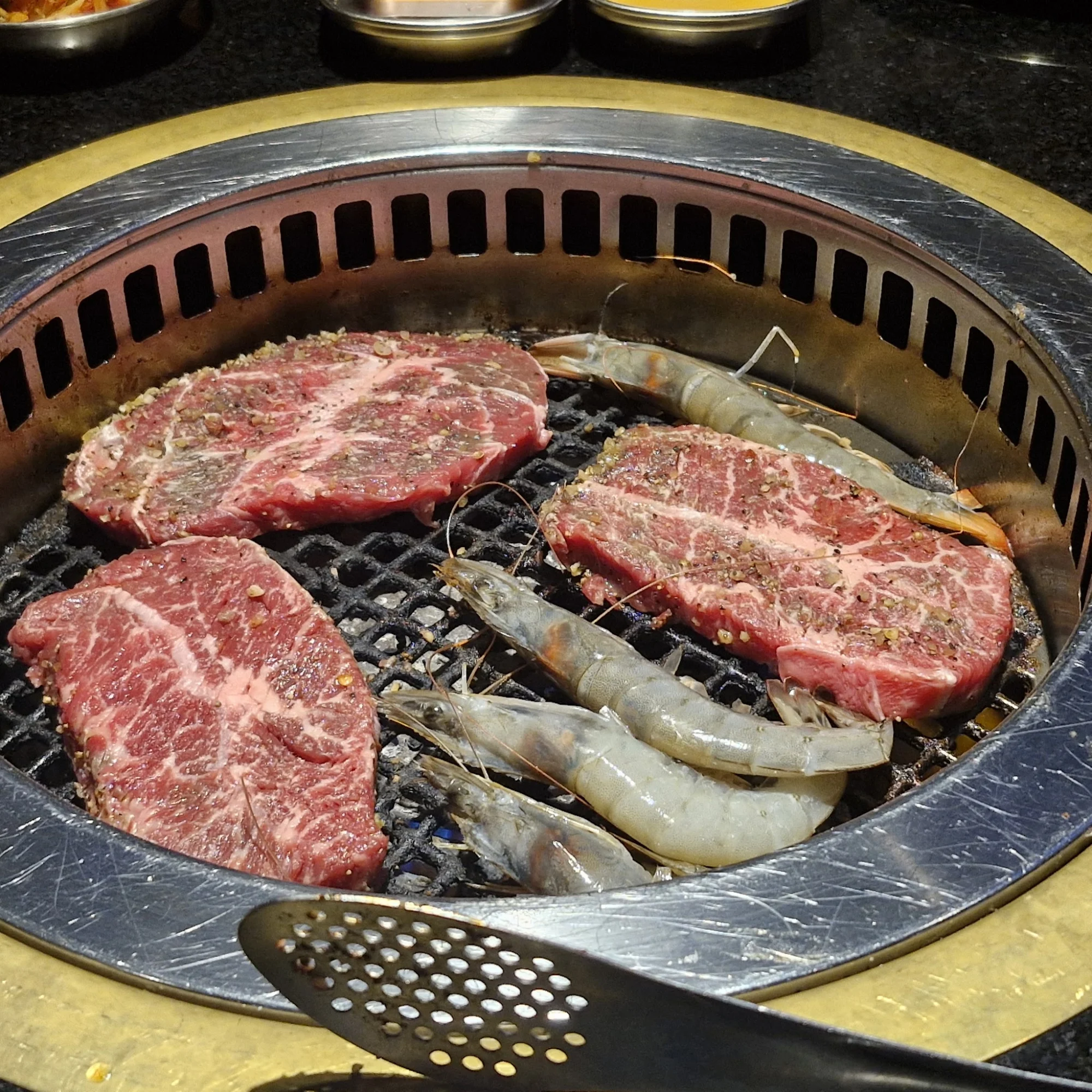 Close-up of steak and shrimp grilling on a metal grill at Iron Age Korean Steakhouse, Rego Park.