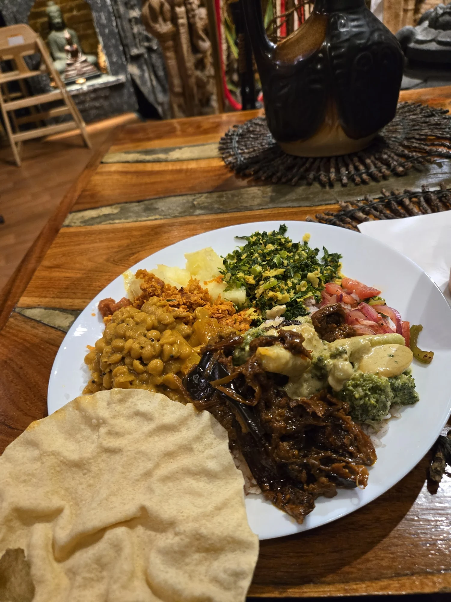 Plate with assorted foods including legumes, greens, meats, and a poppadom at Lakruwana Restaurant, Stapleton.